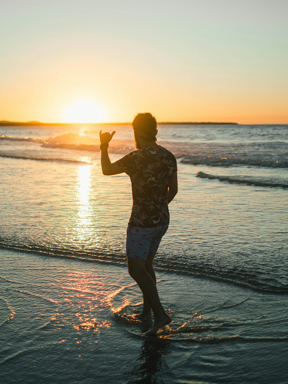 man in black and white floral shirt standing on beach during sunset