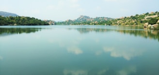 A serene landscape with a calm lake reflecting the sky, surrounded by gentle hills.
