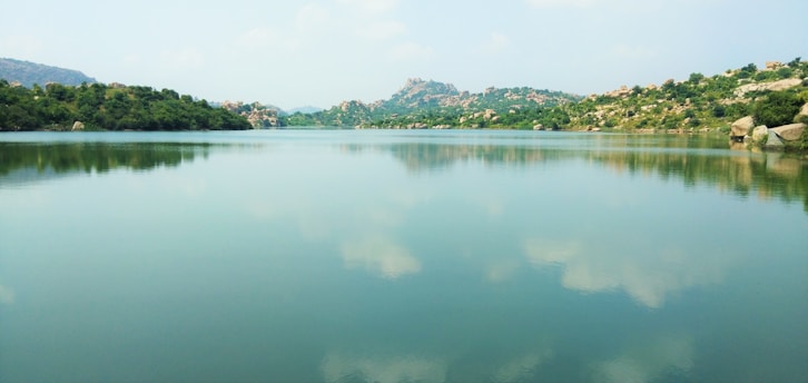 A serene landscape with a calm lake reflecting the sky, surrounded by gentle hills.