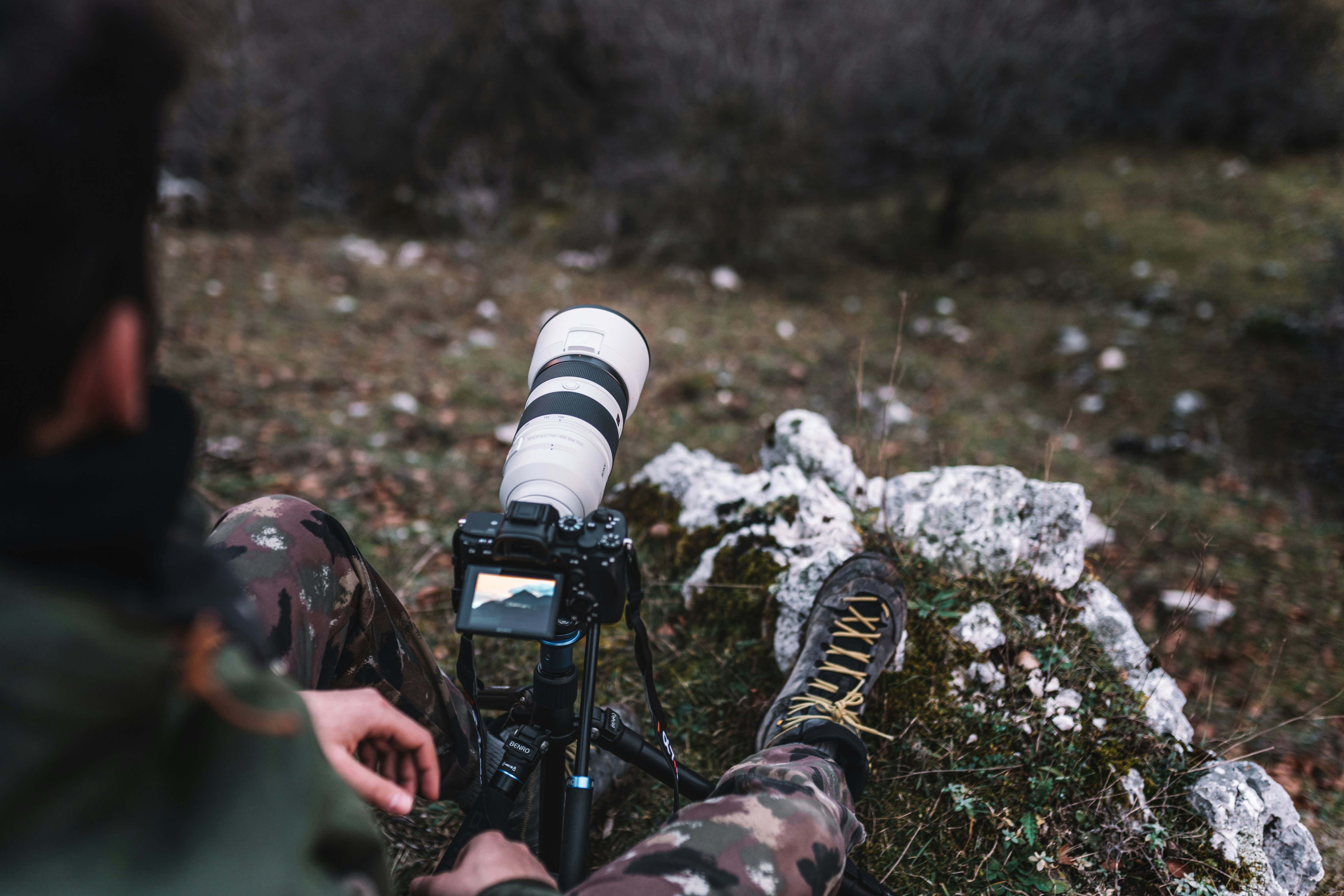 man in camouflage jacket holding black dslr camera
