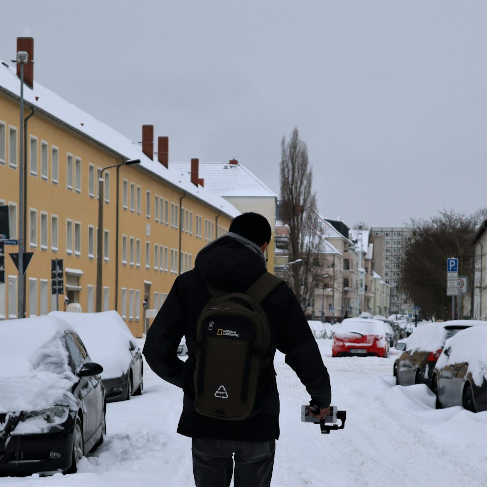 man in black jacket and black backpack walking on snow covered road during daytime