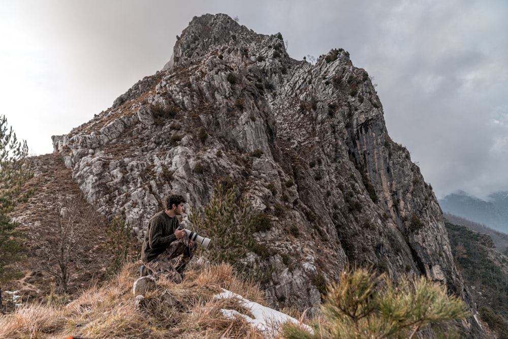 Uomo in giacca nera che si siede sulla montagna rocciosa durante il giorno