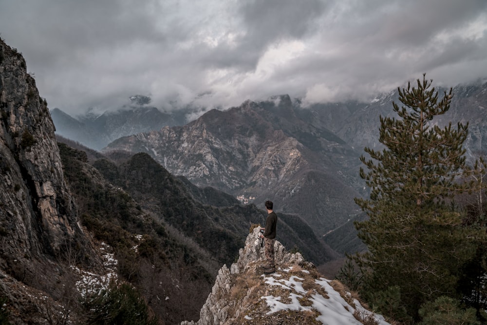 pessoa na jaqueta preta de pé na montanha rochosa durante o dia