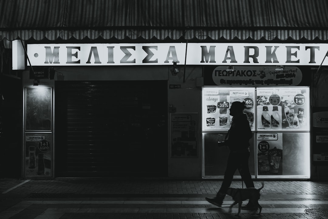 grayscale photo of woman in black coat walking on sidewalk