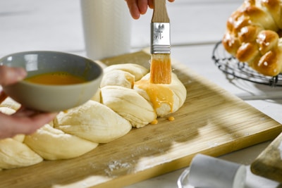 A hand brushing egg wash on the edges of puff pastry squares before baking