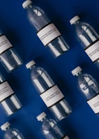 Several empty plastic bottles with labels are arranged diagonally on a deep blue background. The labels on the bottles contain text related to the environmental impact of plastic pollution.