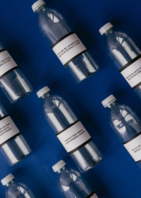 Several empty plastic bottles with labels are arranged diagonally on a deep blue background. The labels on the bottles contain text related to the environmental impact of plastic pollution.