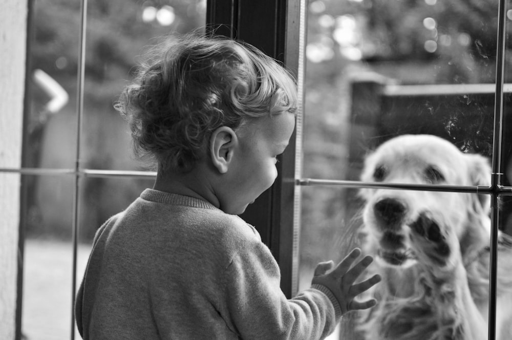 grayscale photo of girl in sweater holding dogs face