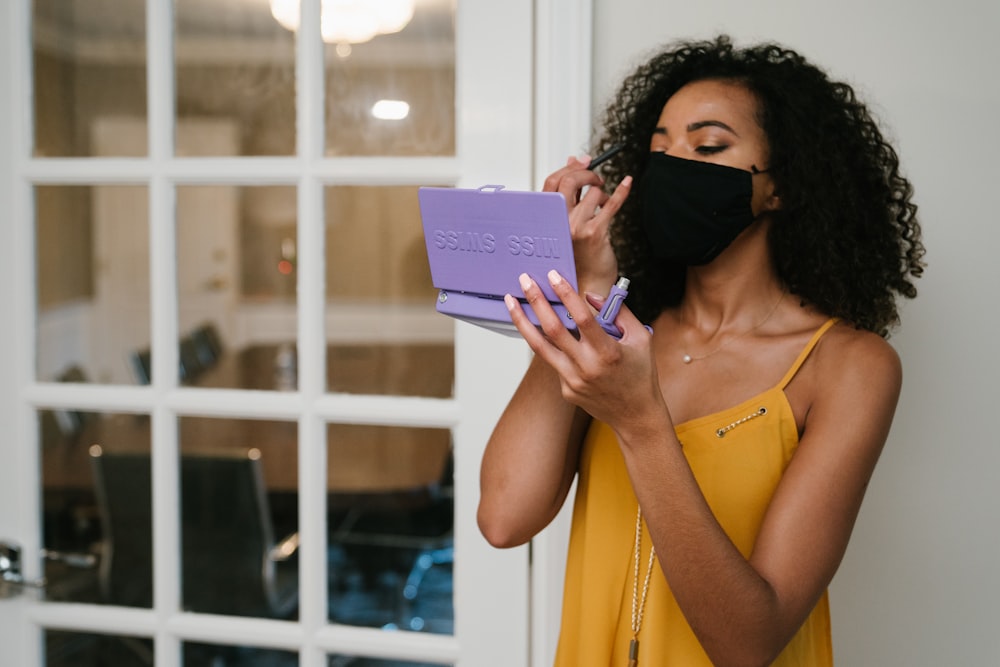 Donna in canottiera gialla che tiene il computer tablet viola