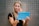 A person with long blonde hair is applying makeup using a blue folding mirror labeled 'MISS SWISS'. They hold the mirror in one hand and a makeup tool in the other. The background features a gray, perforated wall.