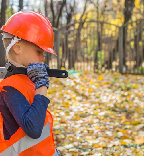 boy in orange and black jacket wearing red helmet holding black dslr camera