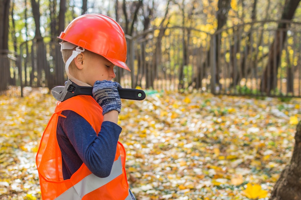 boy in orange and black jacket wearing red helmet holding black dslr camera