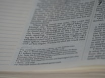 A close-up view of a page from the Bible with text covering a religious passage. The focus is on the middle of the page with clear text, while the sides of the page gradually become out of focus. The passage seems to relate to the story of King David.