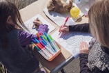 two young girls sitting at a table with markers and crayons