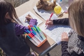 two young girls sitting at a table with markers and crayons