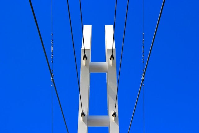 A modern structure featuring a white pillar with multiple cables attached, set against a clear blue sky.