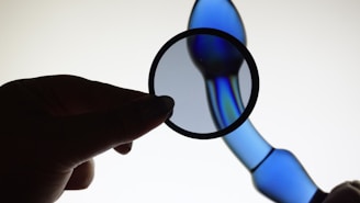A hand holds a circular polarizing filter against a continuous gradient of blue light. The background features a smooth, abstract blue form that appears to be a glass or plastic structure with reflective surfaces and gentle curves.