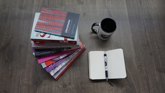A stack of books on economics with a notepad and pen.