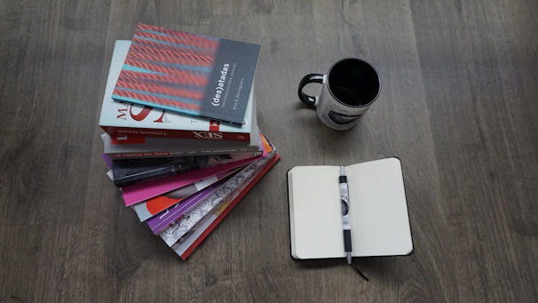 A stack of colorful books with handwritten notes and a steaming cup of tea beside them.