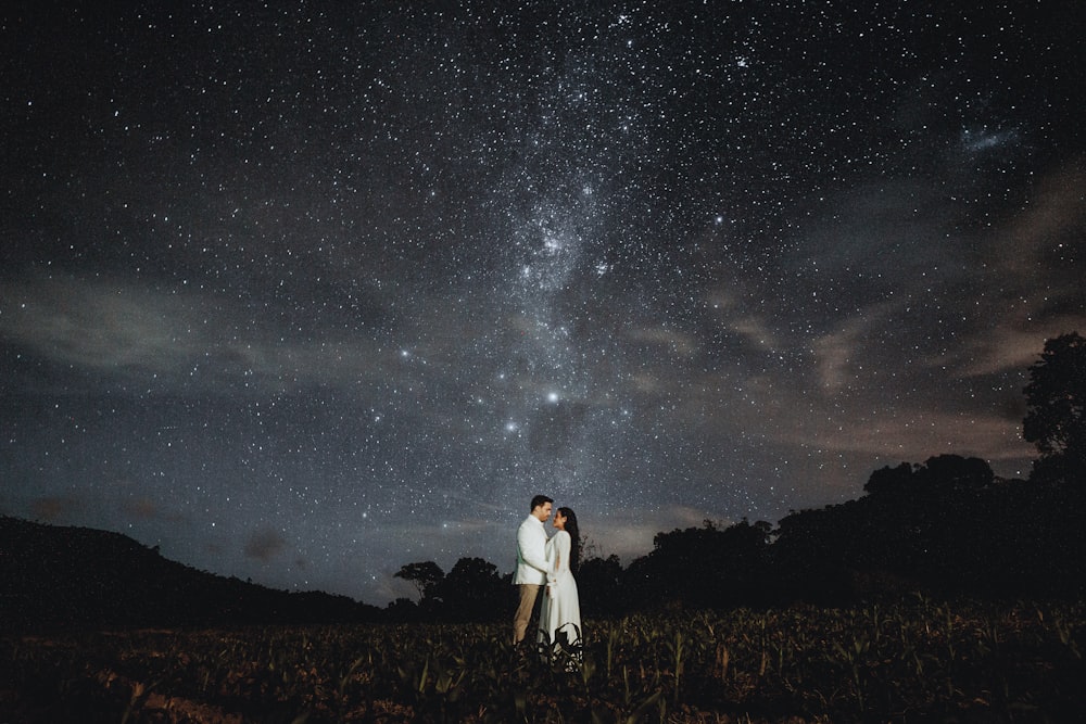 man and woman standing on brown grass field under starry night