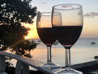 A serene scene of a single wine bottle and glass resting on a windowsill overlooking a peaceful vineyard at sunset.