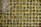 A grid of small, square, ceramic tiles featuring a textured surface. The tiles display a variety of earthy tones, including shades of green, brown, and yellow, with occasional glossy highlights from reflections.
