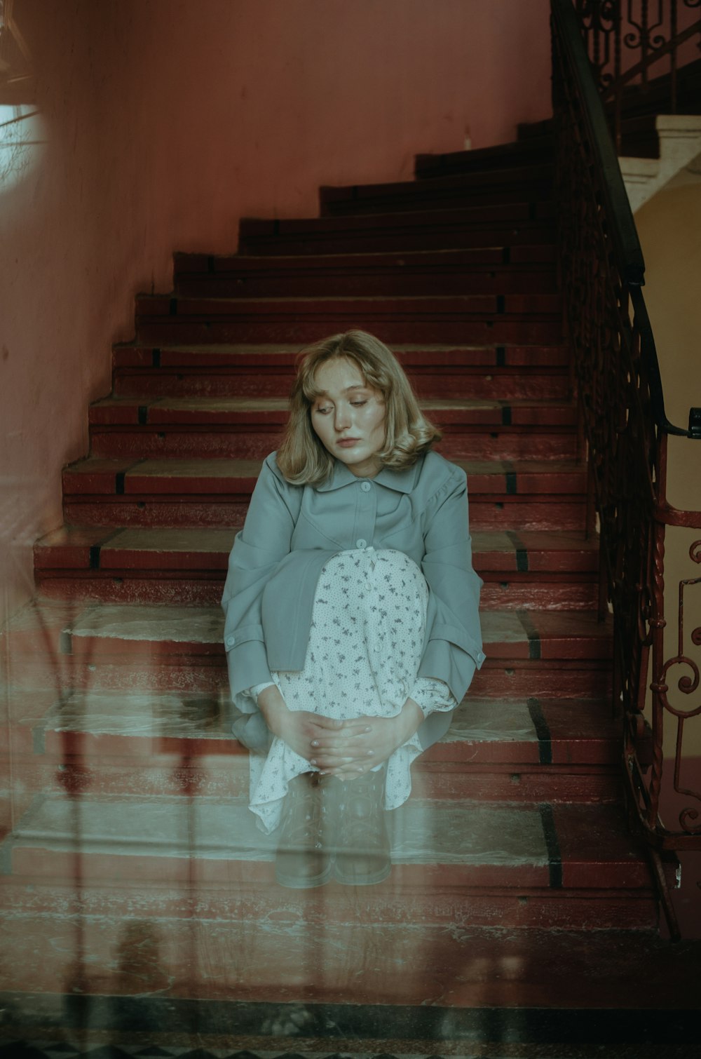 girl in pink long sleeve shirt and white skirt sitting on brown wooden staircase