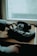 A rotary dial telephone is placed on a wooden surface near a window. A person's hand is reaching towards the dial of the vintage phone. The scene is dimly lit, suggesting an old-fashioned or nostalgic setting.