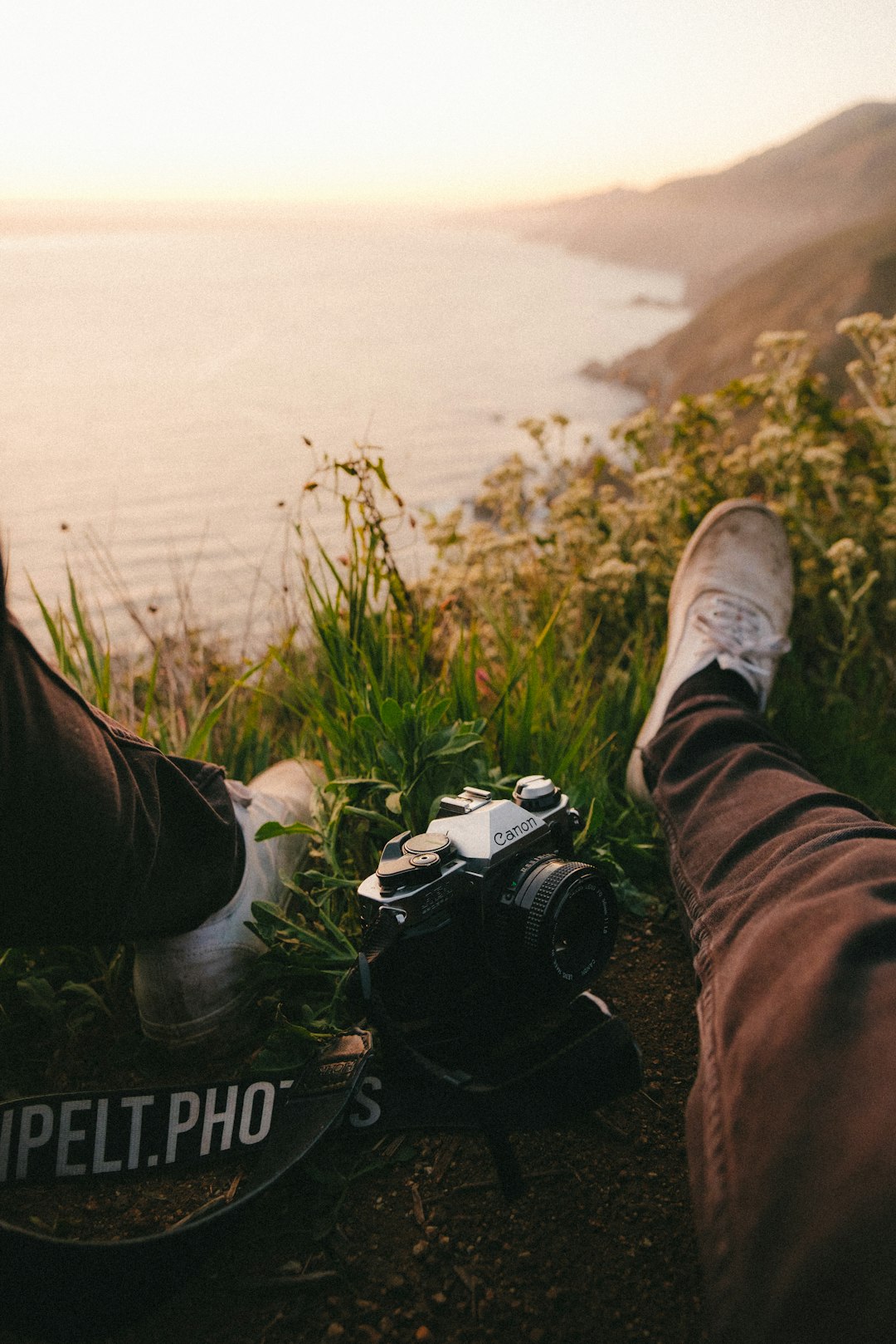 person in black pants and white sneakers sitting on grass field with black and white dslr