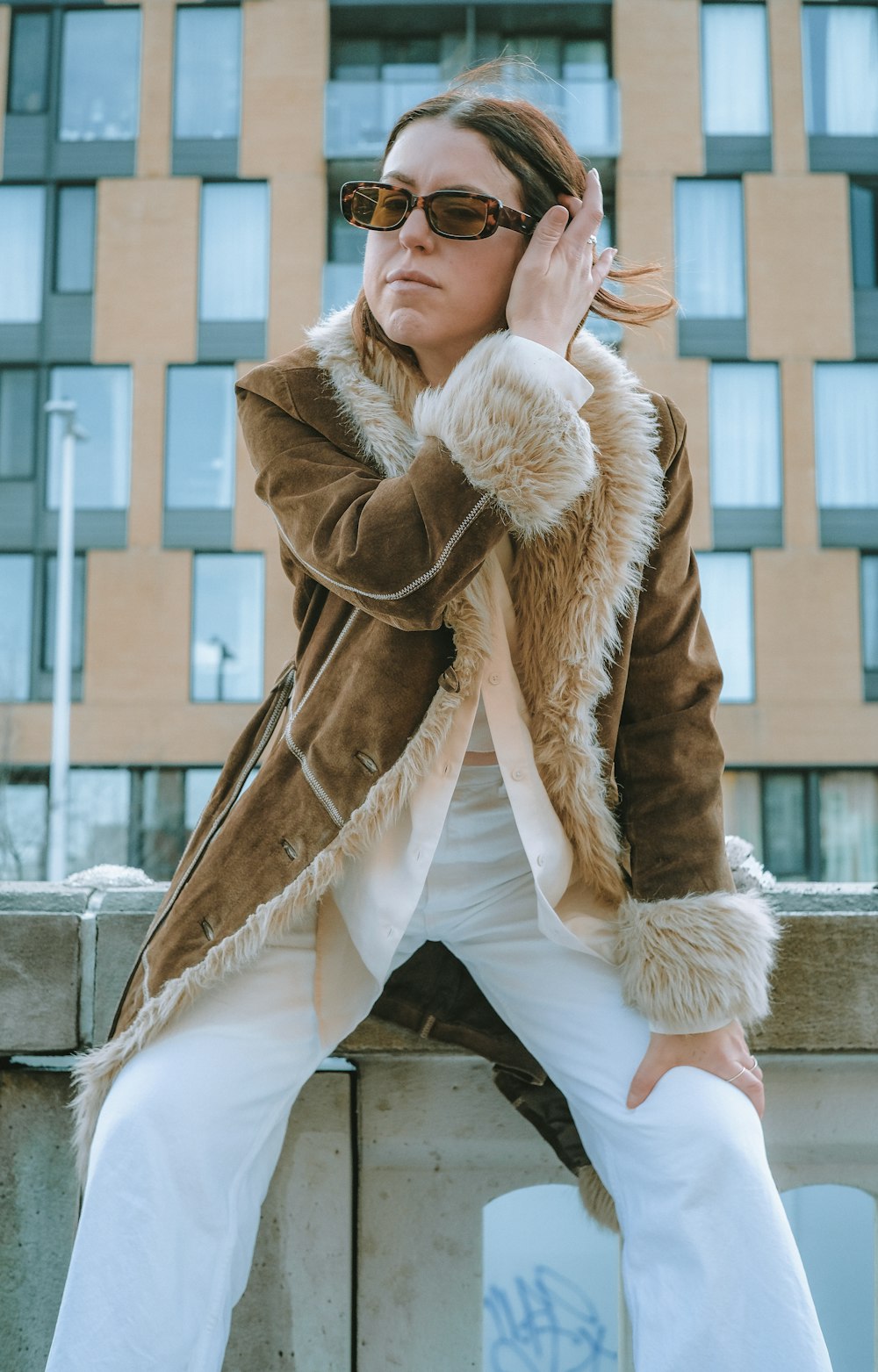woman in brown fur coat and white pants sitting on brown wooden bench