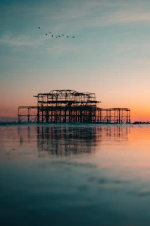 silhouette of dock on body of water during sunset