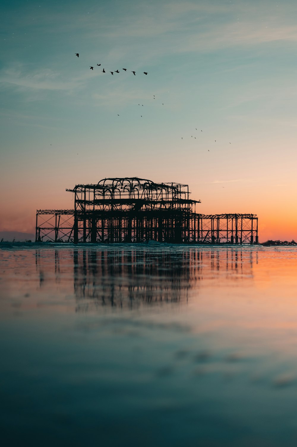 silhouette of dock on body of water during sunset