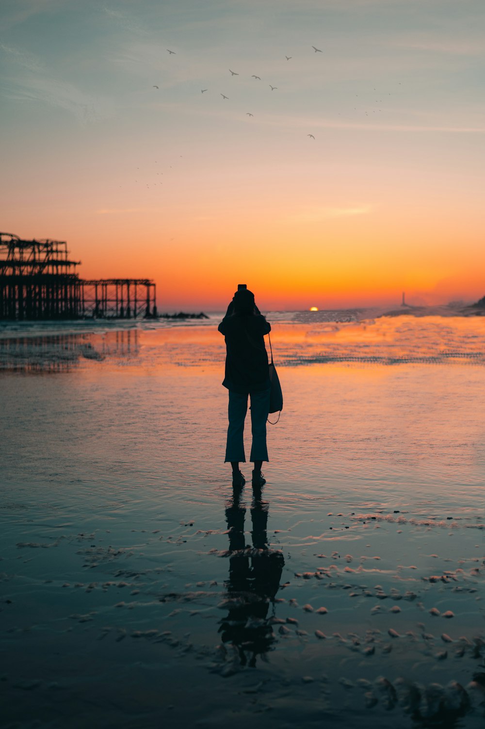 Silueta de mujer de pie en la playa durante la puesta del sol