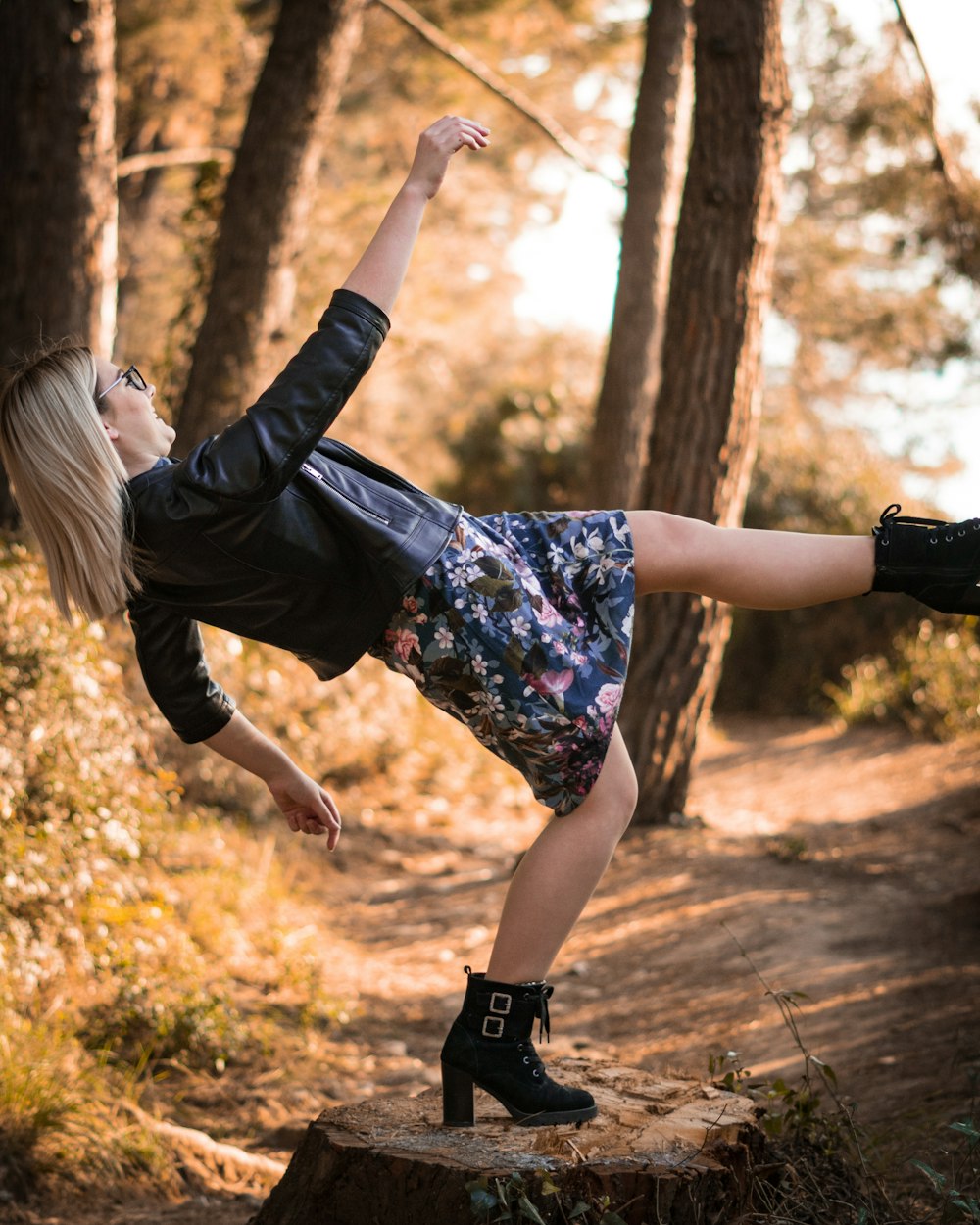 Frau in schwarz-blauem Blumenkleid, die tagsüber auf braune getrocknete Blätter springt