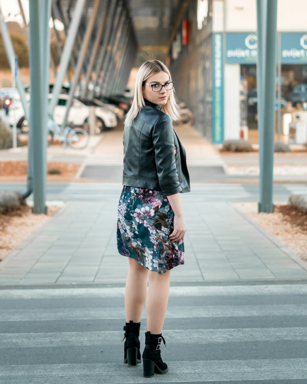 woman in black leather jacket standing on sidewalk during daytime