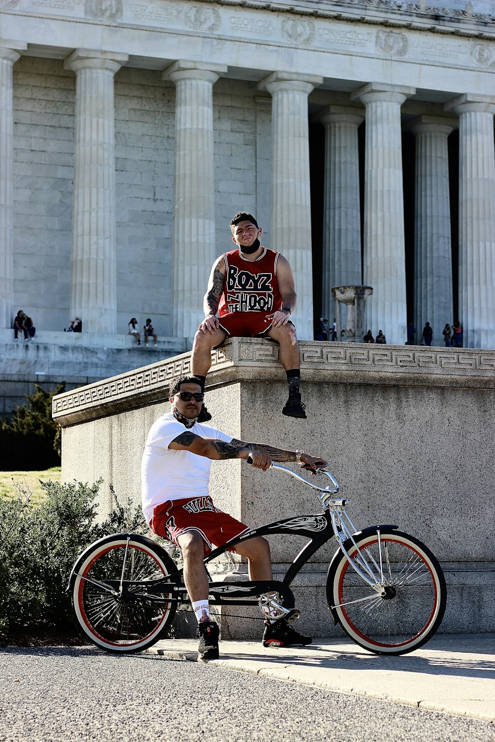 昼間、赤い自転車に乗った赤と白のタンクトップを着た男性