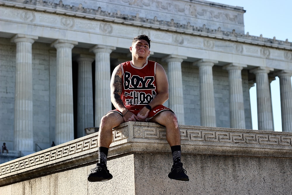 man in red and white tank top sitting on concrete bench during daytime