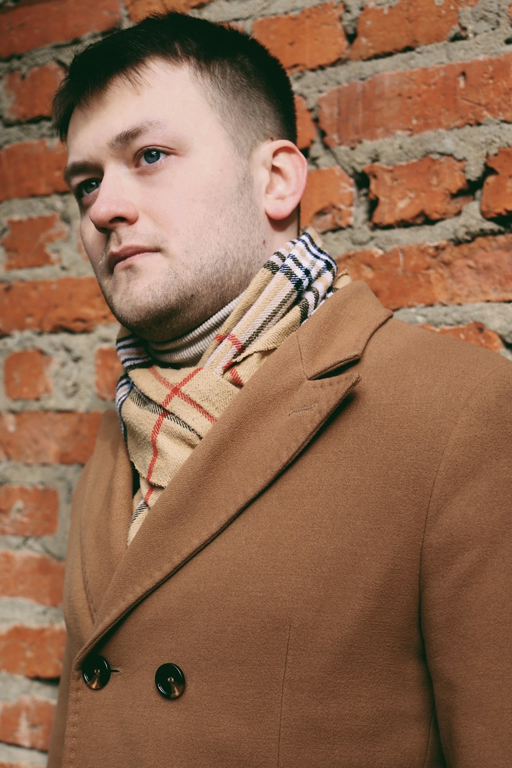man in brown coat standing near brown brick wall