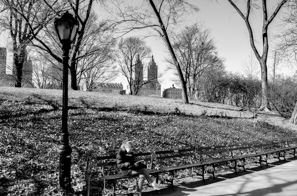 grayscale photo of man and woman sitting on bench near bare trees