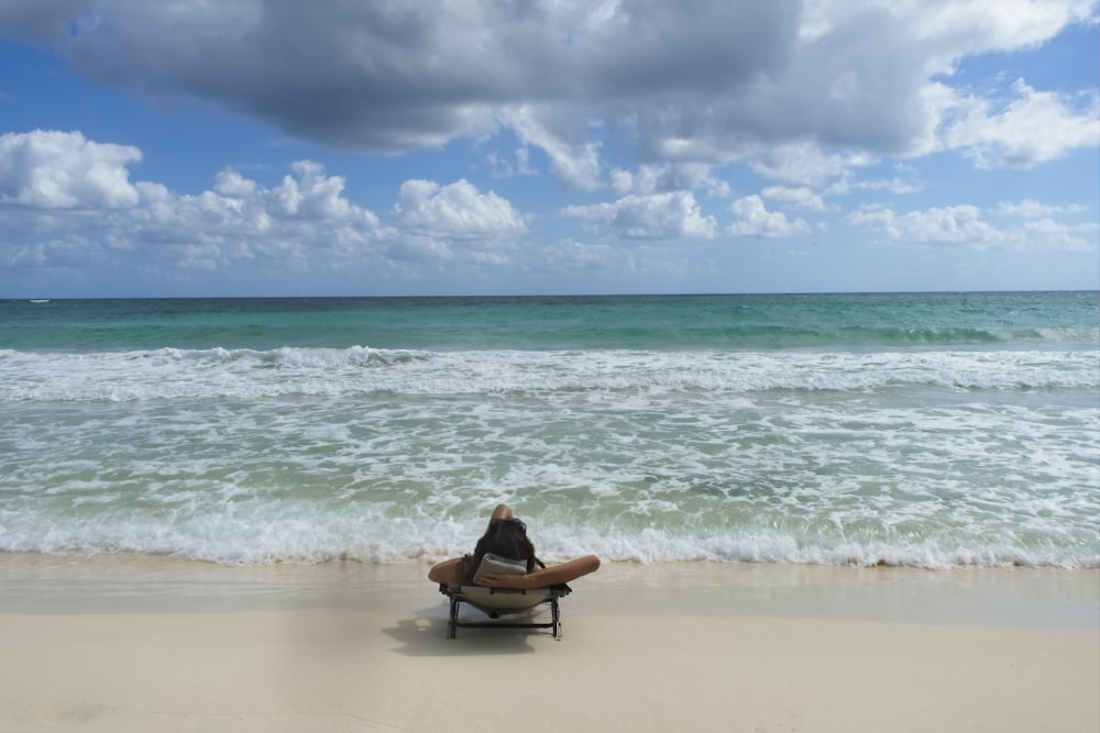 femme en chemise rouge assise sur un bateau en bois marron sur la plage pendant la journée