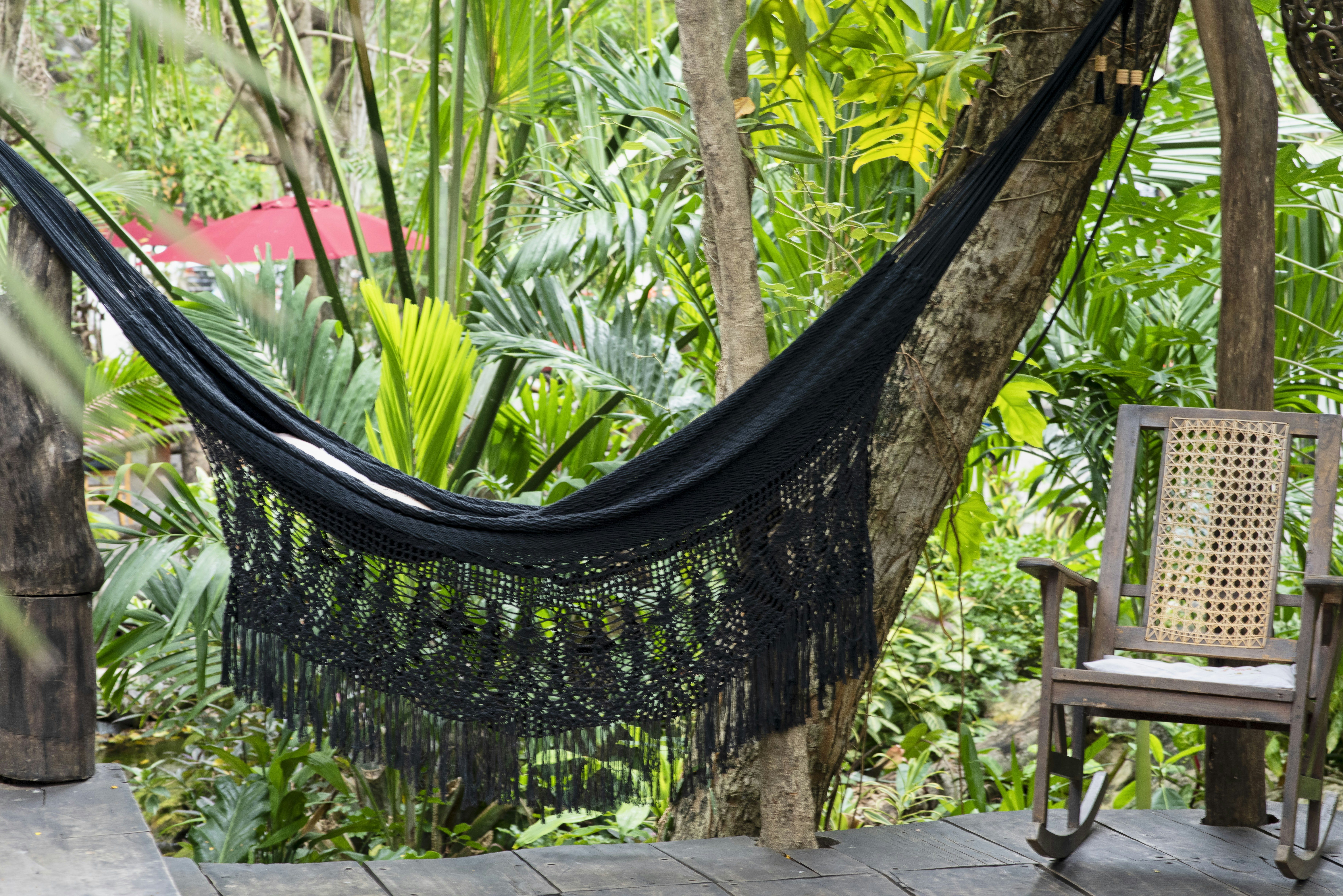 A woven hammock and rocking chair sit on a wooden deck.