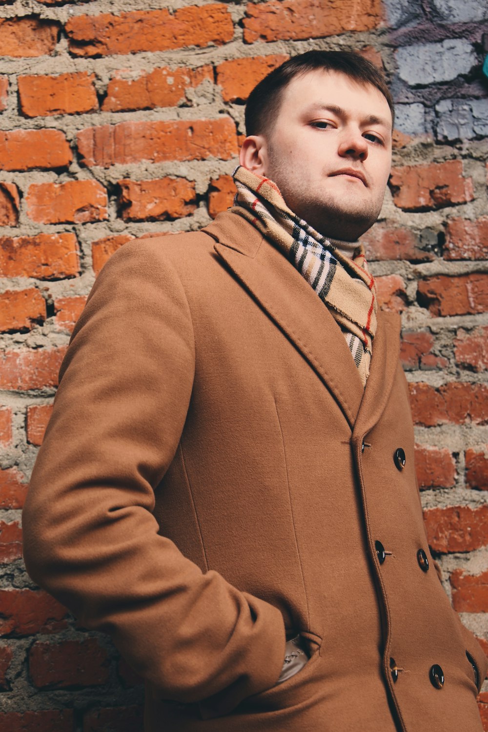 man in brown coat standing beside brown brick wall