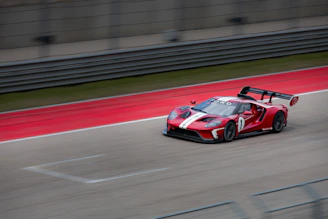 Side view of a red car with custom black and white racing stripes speeding down a track.