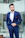 A sharply dressed man in a tailored navy suit standing confidently against a sleek urban backdrop.
