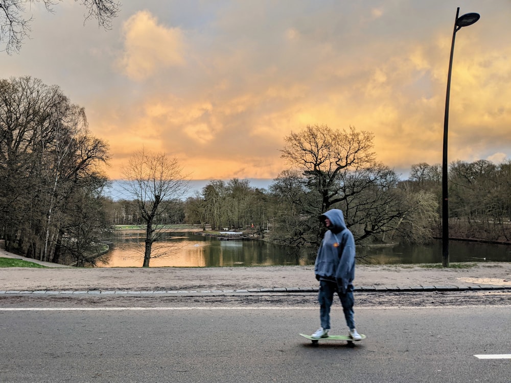 man in blue jacket standing on gray concrete road near body of water during daytime