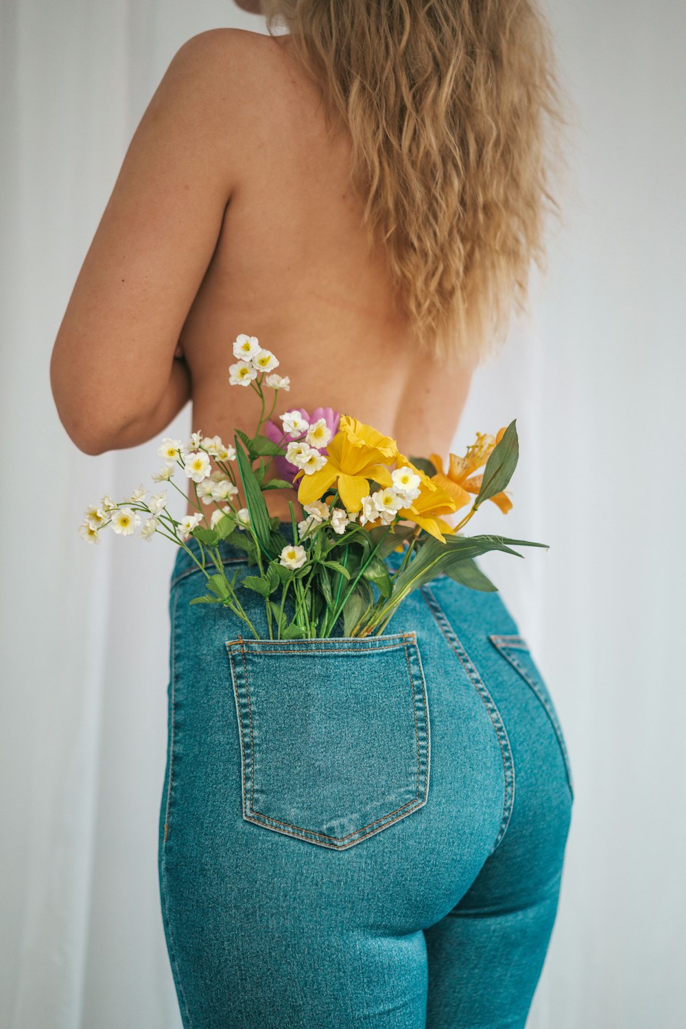 Mujer en falda de mezclilla azul sosteniendo flor amarilla