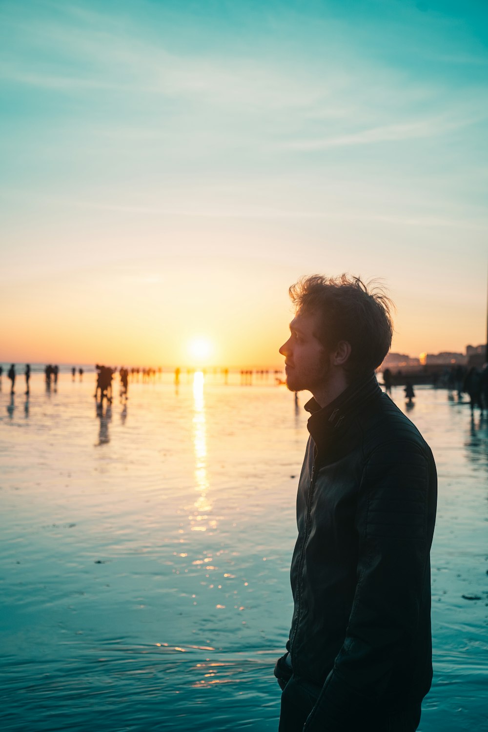 man in black jacket standing on beach during sunset