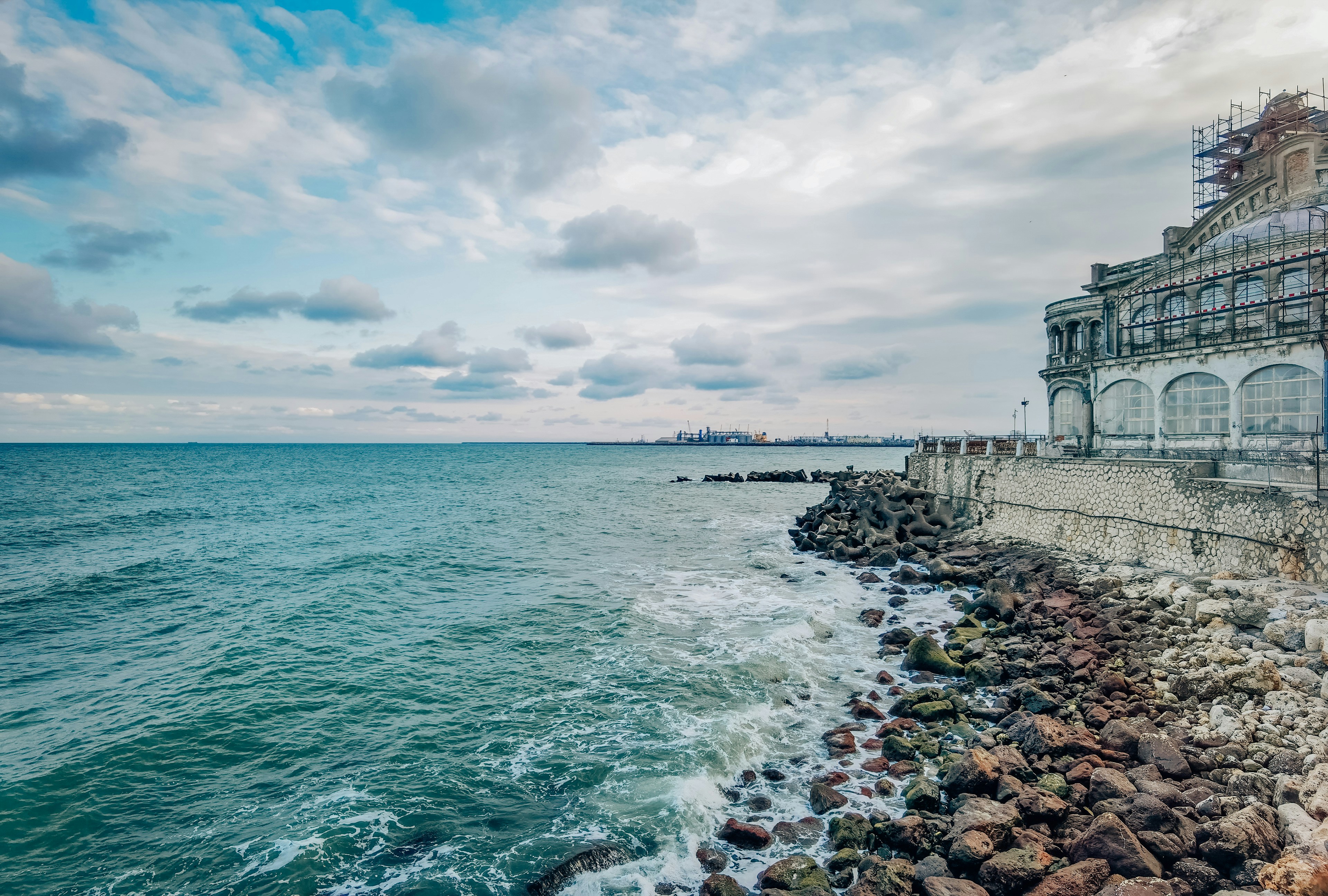 white concrete building near sea under white clouds and blue sky during daytime