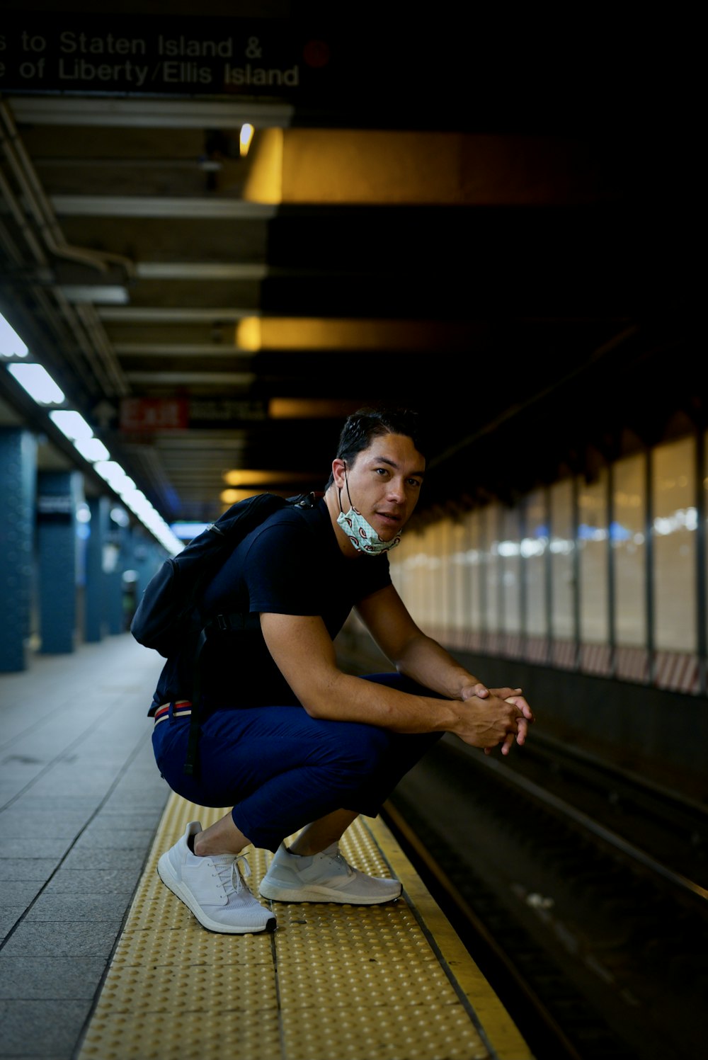 man in black t-shirt and blue denim jeans sitting on train station