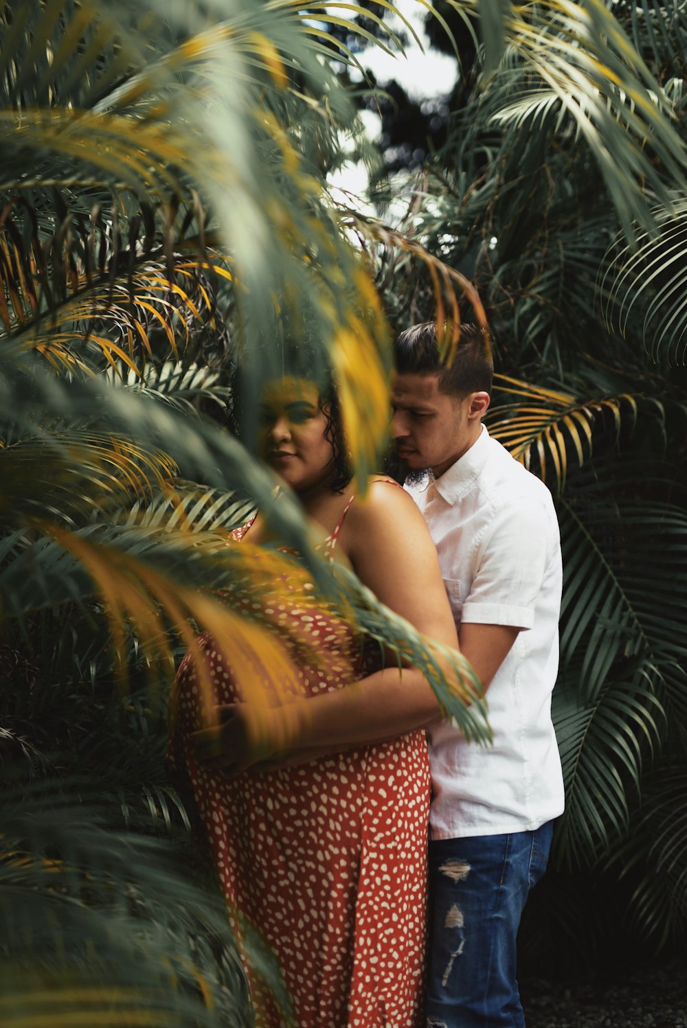 man in white shirt hugging woman in red and brown dress